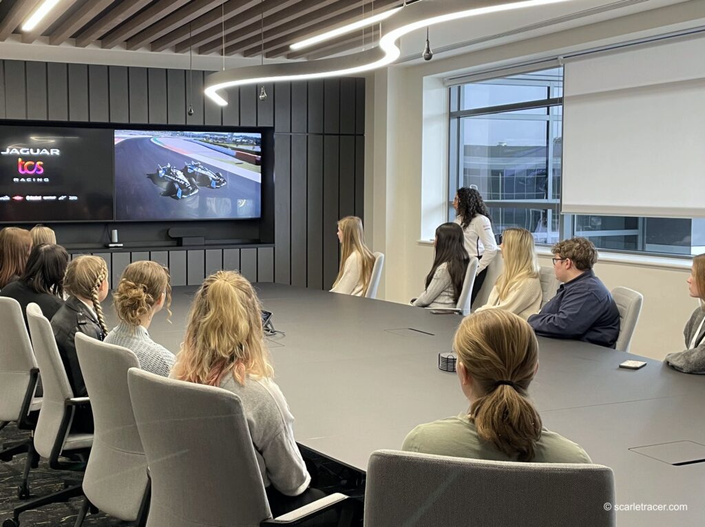 Group of girls gathered around a large meeting table, watching a presentation.